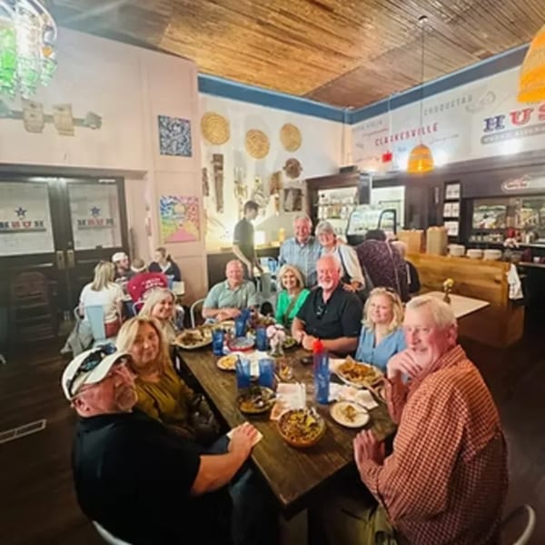 Diners enjoying a meal at a long wooden table inside The Hush Cuban Kitchen restaurant.