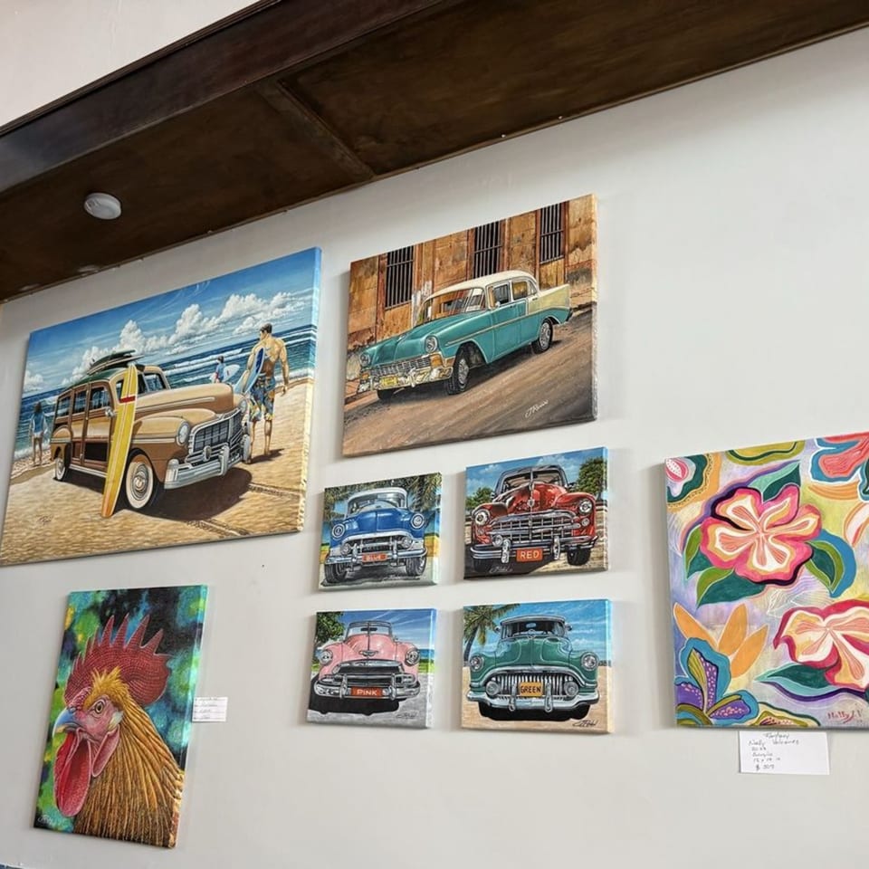 A white wall adorned with vibrant paintings of classic Cuban cars, a rooster, and tropical flowers.