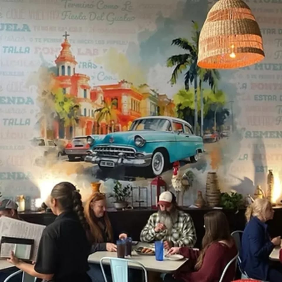 Diners seated at tables in The Hush Cuban Kitchen, with a vibrant mural of a Cuban street scene.