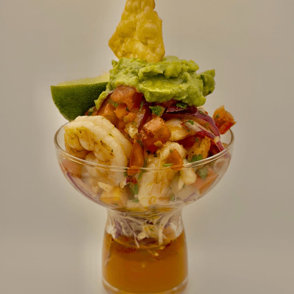 Cuban shrimp ceviche with guacamole, pico de gallo, and a lime wedge in a glass.