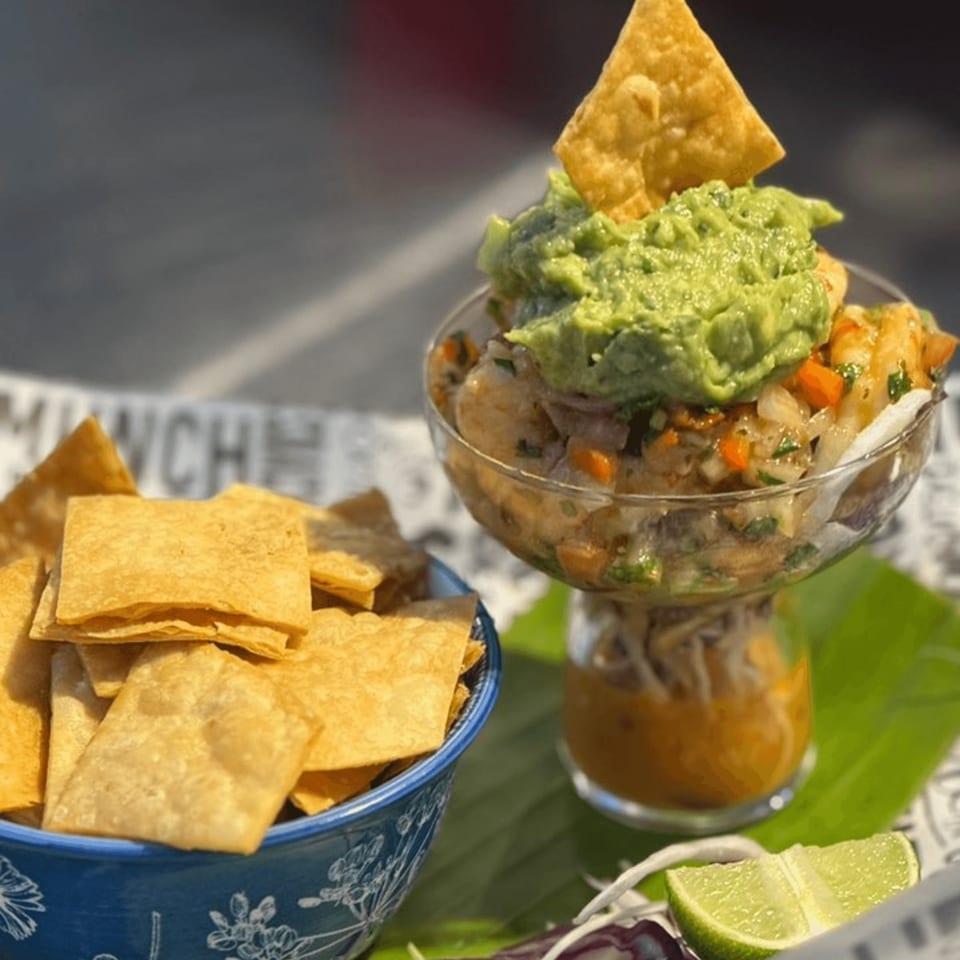 Cuban ceviche with guacamole and a tortilla chip in a glass, next to a bowl of chips.