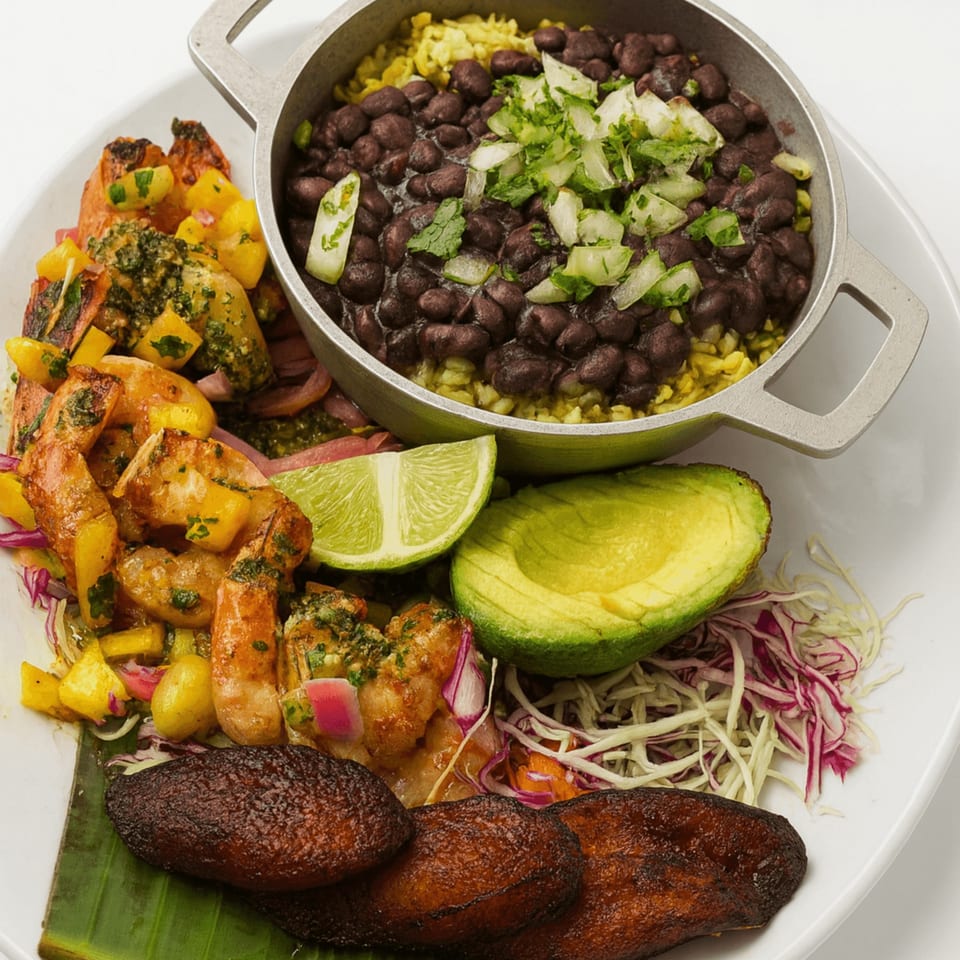 Cuban dish with shrimp, plantains, black beans and rice, avocado, and lime on a white plate.