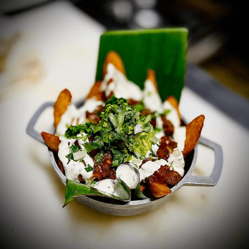 Cuban-style loaded fries with white sauce, meat, guacamole, and cilantro in a metal dish.