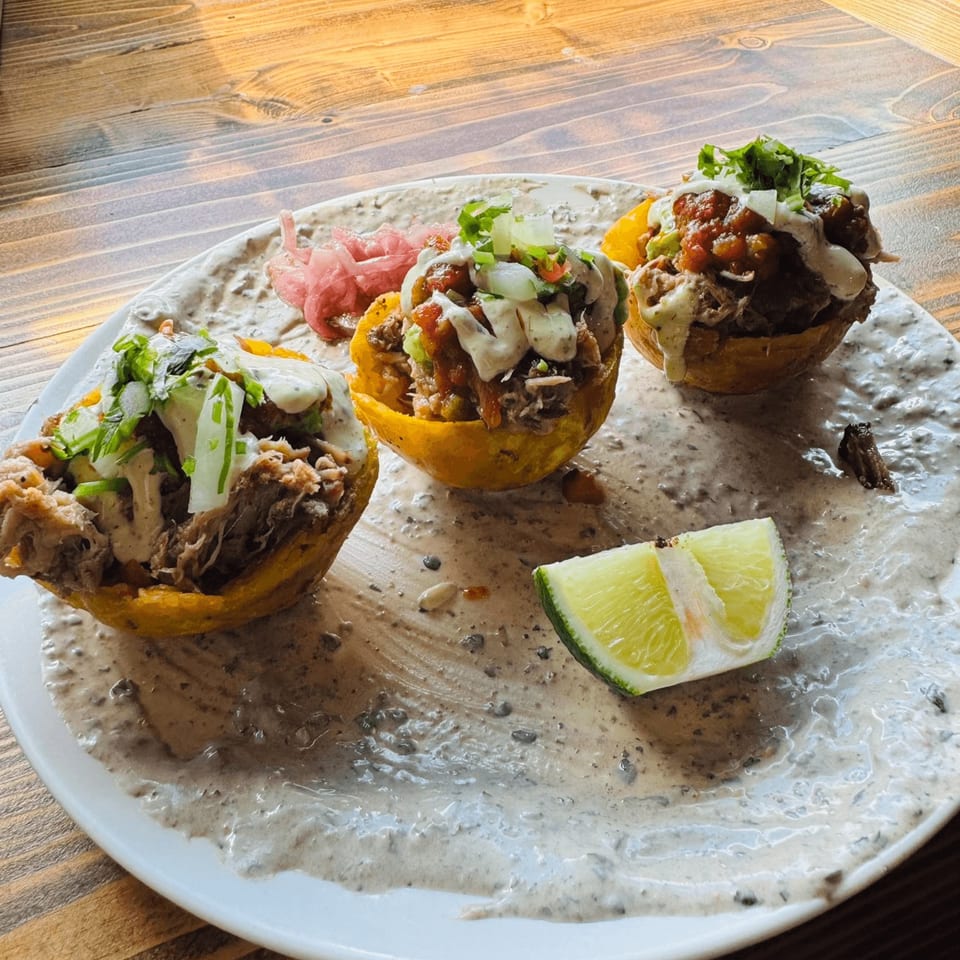 Three Cuban tostones rellenos with shredded meat, salsa, and crema, served with a lime wedge.