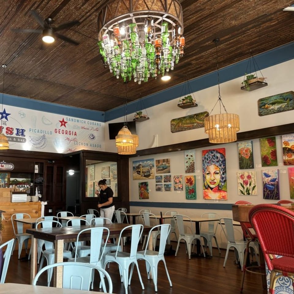 The Hush Cuban Kitchen dining room with light blue chairs, wooden tables, and colorful art on the walls.
