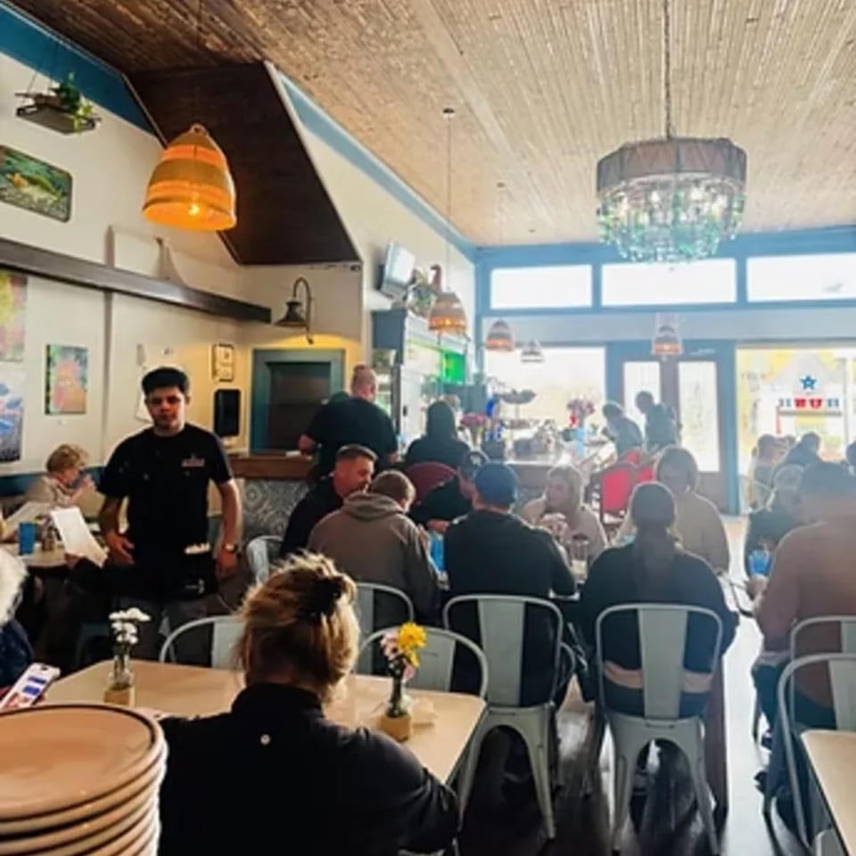 A busy dining room at The Hush Cuban Kitchen, with patrons seated at tables and a waiter standing.